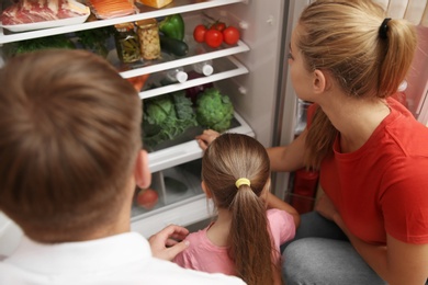 Photo of Young family choosing food in refrigerator at home