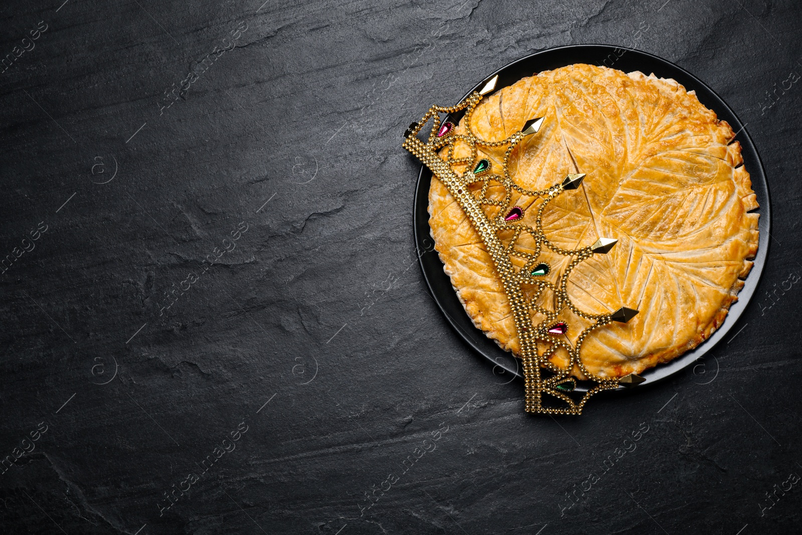 Photo of Traditional galette des rois with crown on black table, top view. Space for text