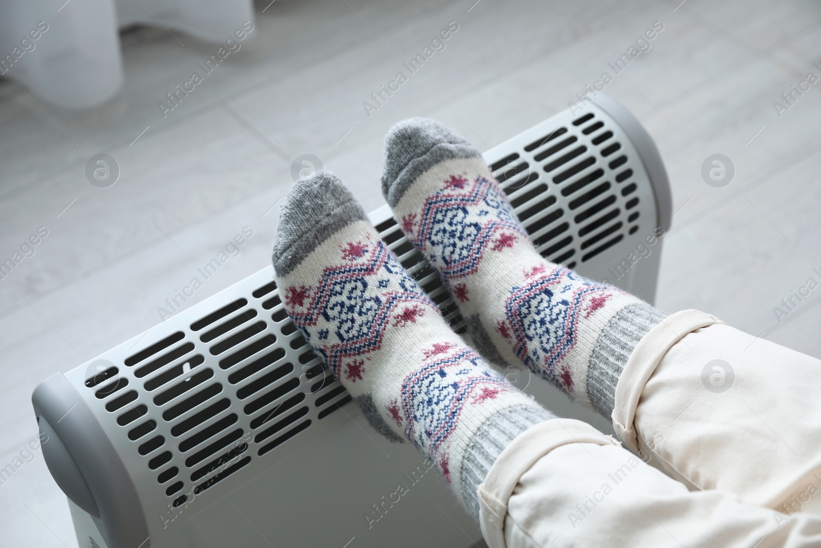 Photo of Woman warming feet on electric heater at home, closeup