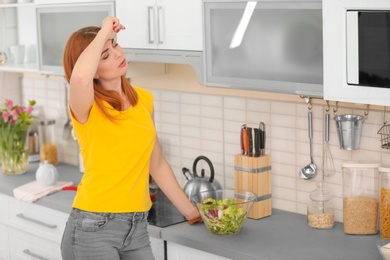 Photo of Tired housewife preparing vegetable salad in kitchen