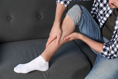 Photo of Man rubbing sore leg on sofa, closeup