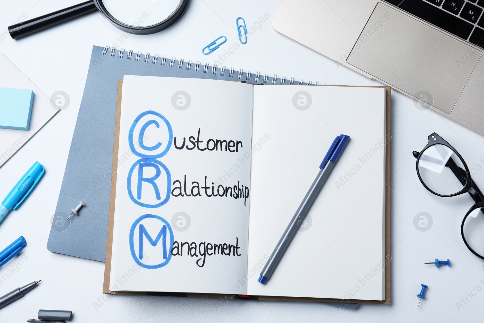 Photo of Notebook with CRM abbreviation on white office table, flat lay. Customer Relationship Management