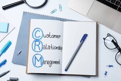 Notebook with CRM abbreviation on white office table, flat lay. Customer Relationship Management
