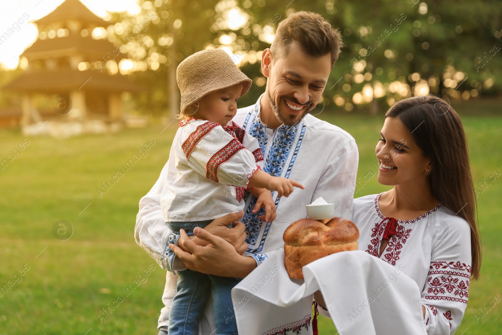 Photo of Happy cute family in embroidered Ukrainian shirts with korovai bread on sunny day. Space for text