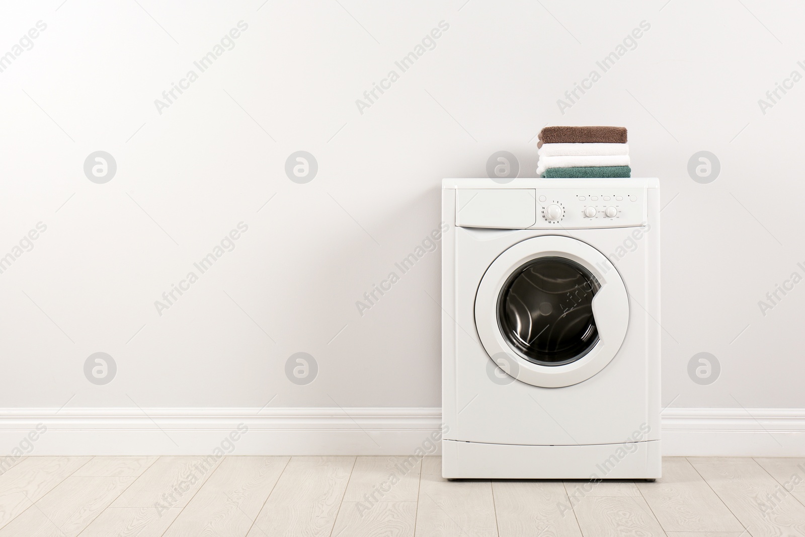 Photo of Modern washing machine with stack of towels near white wall, space for text. Laundry day