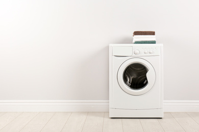 Modern washing machine with stack of towels near white wall, space for text. Laundry day