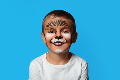 Cute little boy with face painting on blue background