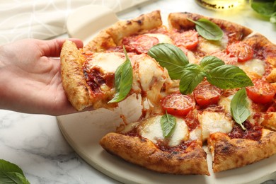 Photo of Woman taking piece of delicious Margherita pizza at white marble table, closeup