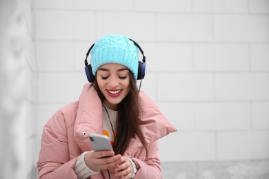 Photo of Beautiful young woman listening to music with headphones near light wall. Space for text