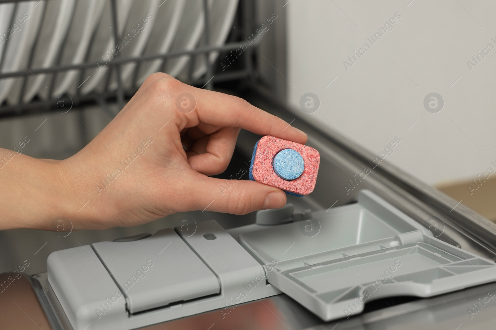 Photo of Woman putting detergent tablet into open dishwasher, closeup