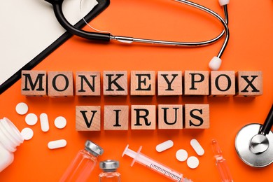 Photo of Flat lay composition with words Monkeypox Virus made of wooden cubes and medical supplies on orange background