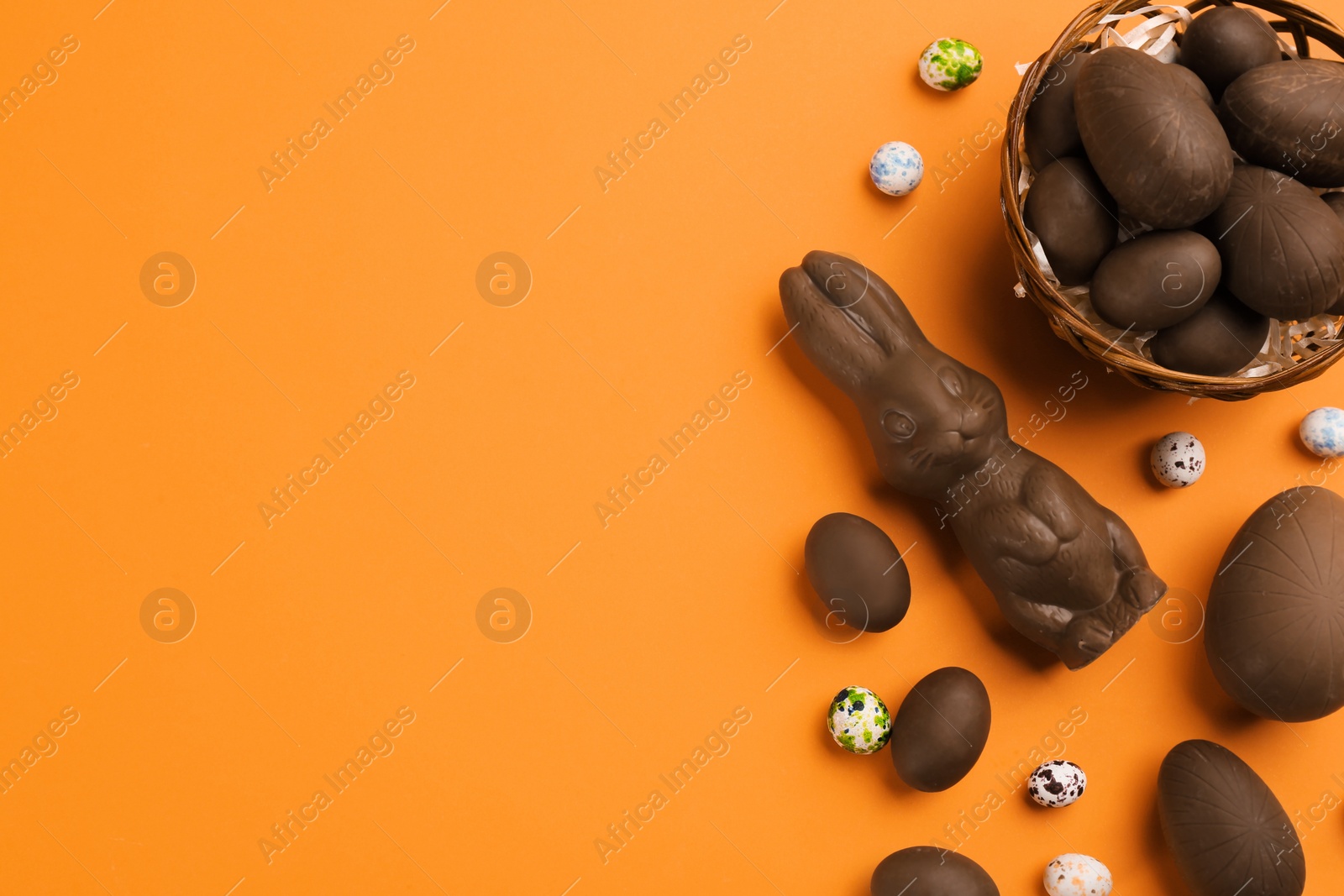 Photo of Flat lay composition with chocolate Easter bunny, eggs and candies on orange background. Space for text