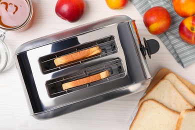 Photo of Toaster with roasted bread, nectarines and jam on white wooden table, flat lay