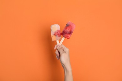 Photo of Woman holding berry popsicles on orange background, closeup