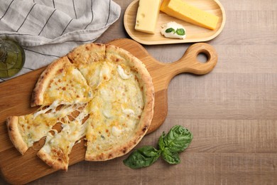 Photo of Delicious cut cheese pizza and ingredients on wooden table, flat lay. Space for text