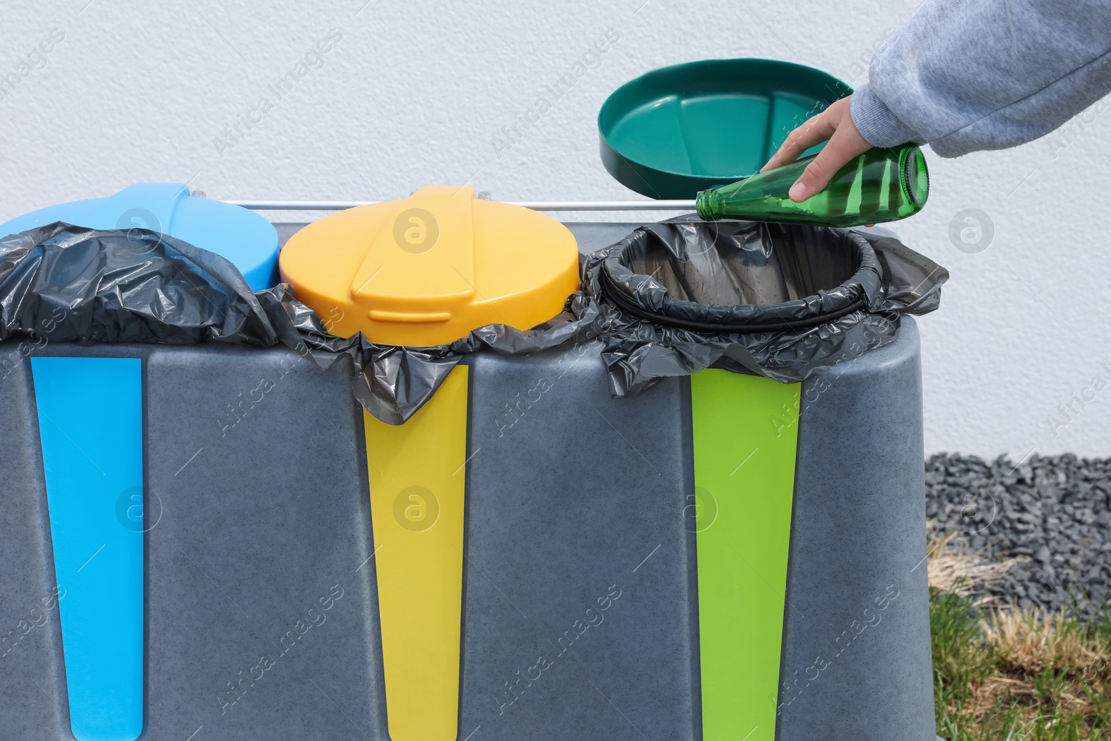 Photo of Woman throwing glass bottle in bin outdoors, closeup. Recycling concept