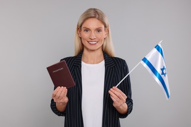 Immigration. Happy woman with passport and flag of Israel on gray background