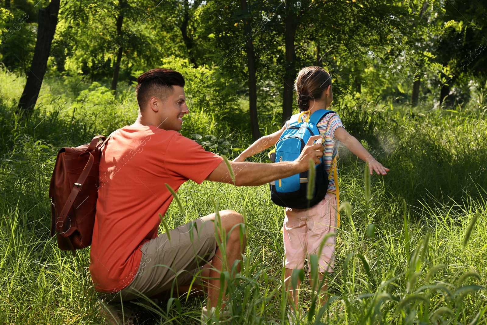 Photo of Father spraying tick repellent on his little daughter's arm during hike in nature