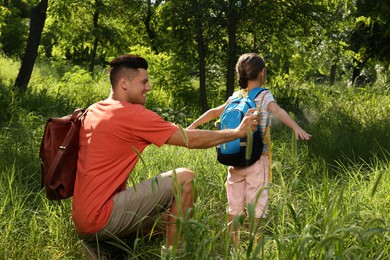 Father spraying tick repellent on his little daughter's arm during hike in nature