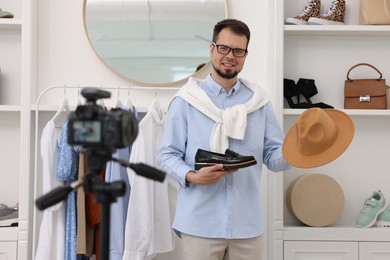 Photo of Smiling fashion blogger showing shoe and hat while recording video at home