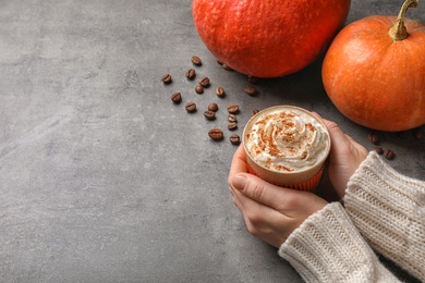 Photo of Woman holding cup of tasty pumpkin spice latte on gray table, closeup with space for text