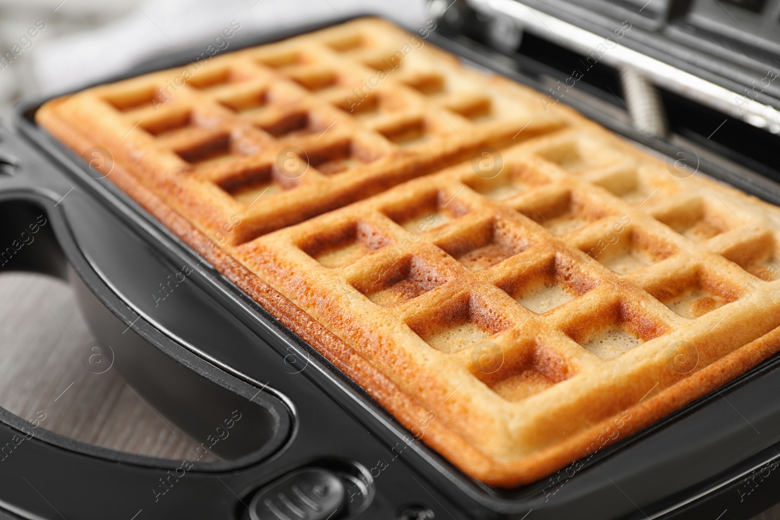 Photo of Modern iron with tasty Belgian waffles on table, closeup