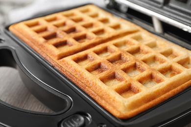 Modern iron with tasty Belgian waffles on table, closeup