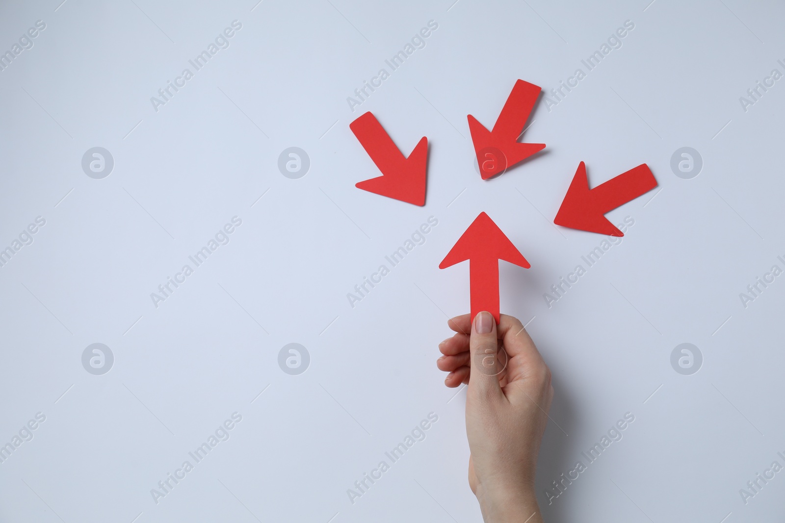 Photo of Woman holding red paper arrow and other arrows pointing at it on white background, top view. Space for text