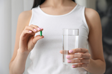 Photo of Woman with glass of water and vitamin capsule on blurred background, closeup