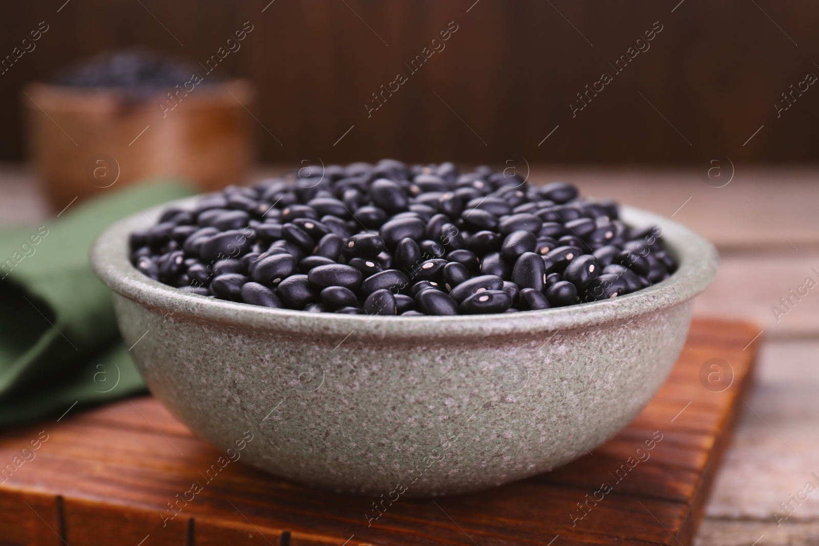 Photo of Bowl of raw black beans on wooden board, closeup