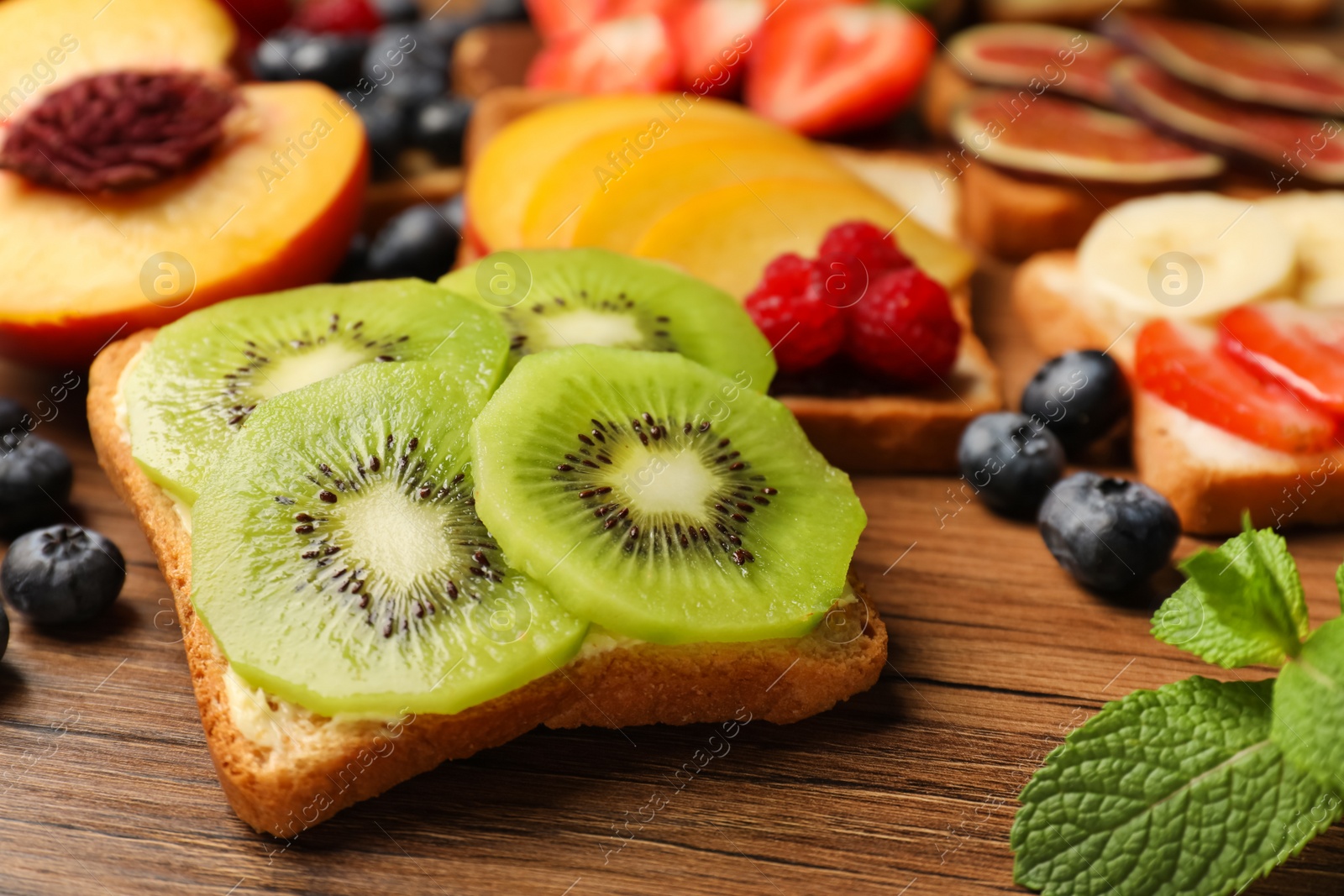 Photo of Tasty toast with butter and kiwi slices on wooden table, closeup
