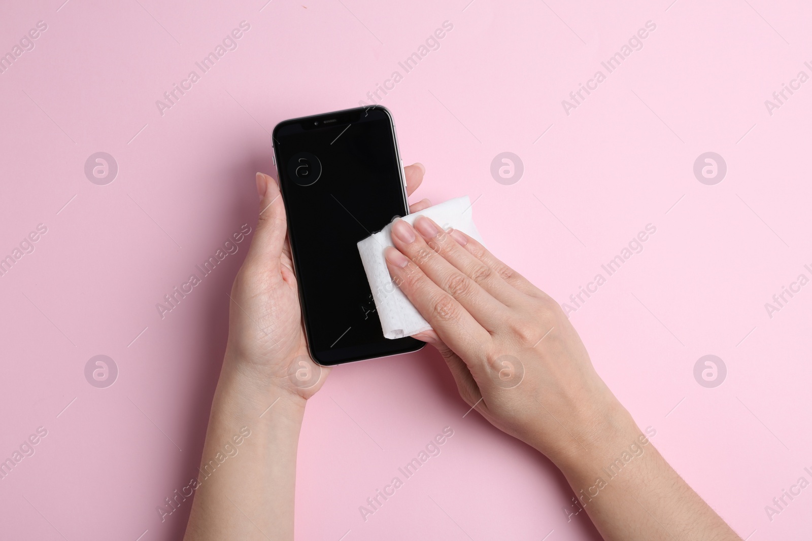 Photo of Woman cleaning mobile phone with antiseptic wipe on pink background, top view