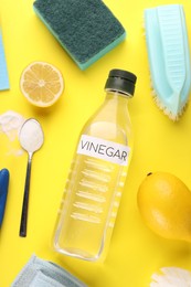 Photo of Eco friendly natural cleaners. Flat lay composition with bottle of vinegar on yellow background