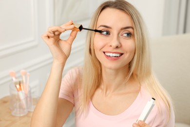 Photo of Beautiful woman applying mascara with brush indoors