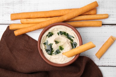 Photo of Delicious hummus with grissini sticks on white wooden table, flat lay