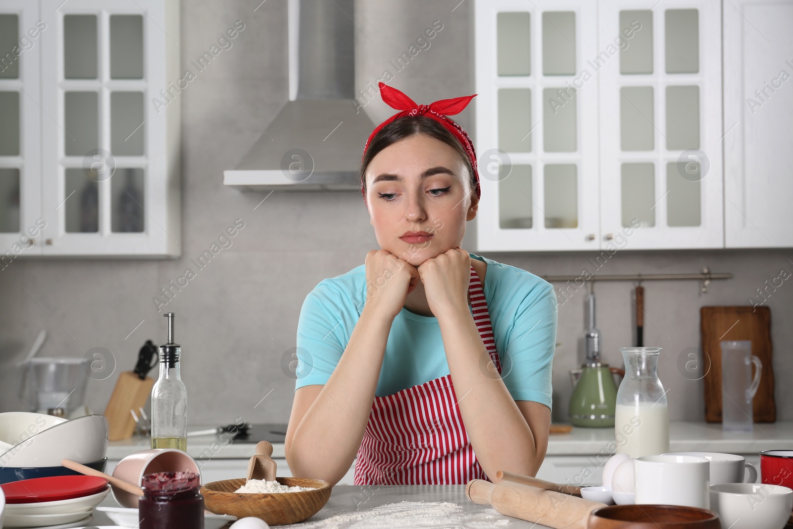 Photo of Upset housewife at messy countertop in kitchen. Many dirty dishware, food leftovers and utensils on table