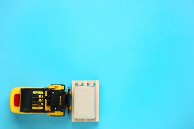 Photo of Toy forklift with wooden pallet and box on light blue background, top view. Space for text