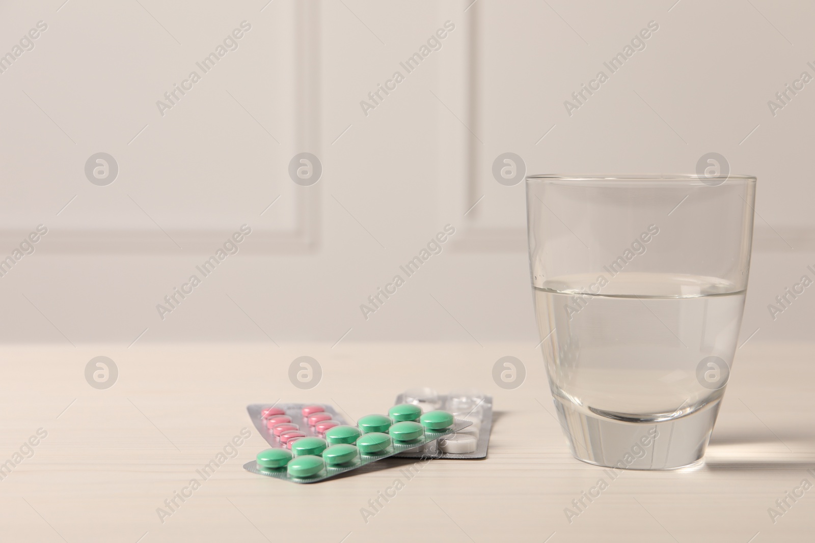 Photo of Different pills in blisters and glass of water on white wooden table. Space for text