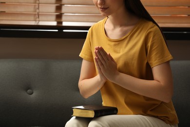 Religious woman praying over Bible indoors, closeup