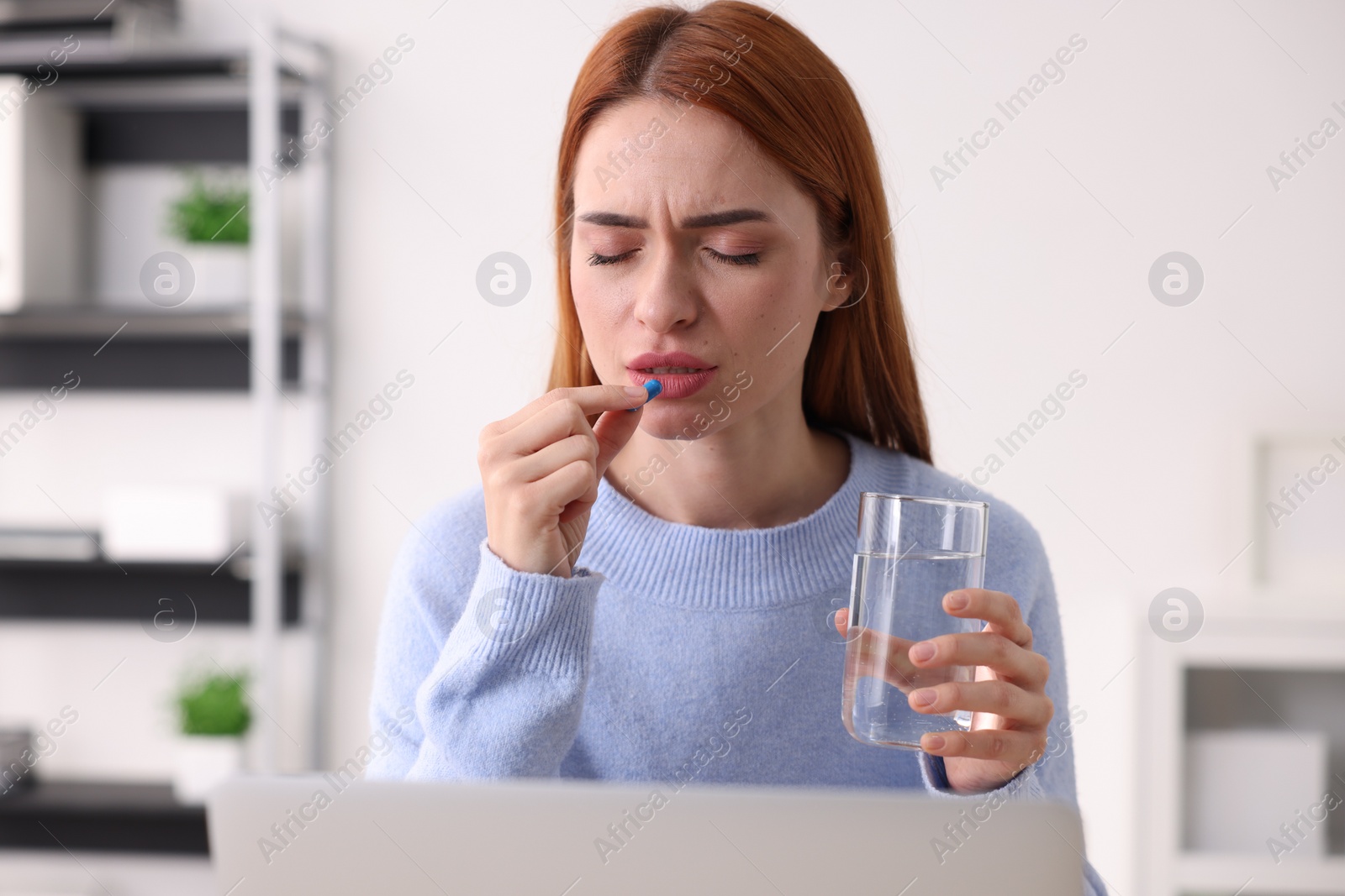 Photo of Woman with pill and glass of water suffering from headache at workplace in office