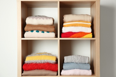 Photo of Stacks of folded winter clothes on shelves in wardrobe