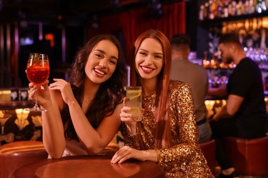 Happy young women with fresh cocktails at table in bar