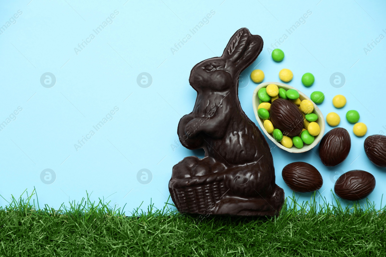 Photo of Chocolate Easter bunny, eggs and candies with green grass on light blue background. Space for text