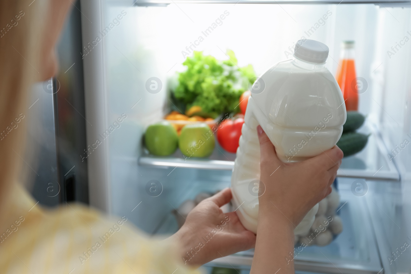 Photo of Young woman putting gallon of milk into refrigerator indoors, closeup