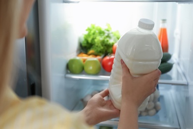 Young woman putting gallon of milk into refrigerator indoors, closeup