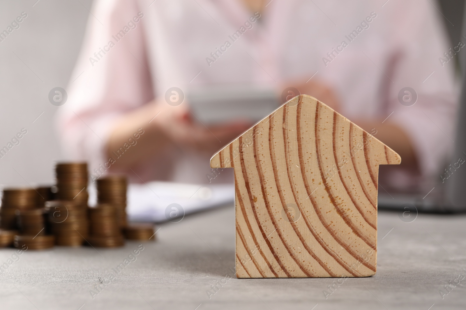 Photo of Woman calculating money at grey table, focus on wooden house model