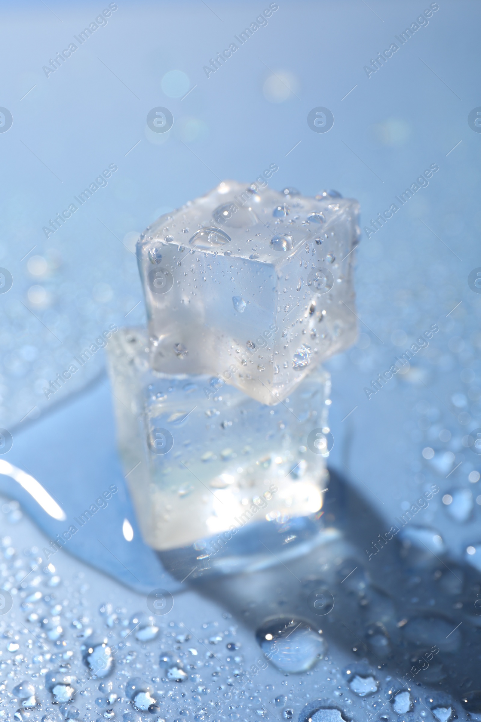 Photo of Melting ice cubes and water drops on light blue background, closeup