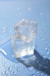 Melting ice cubes and water drops on light blue background, closeup