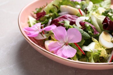 Fresh spring salad with flowers on grey table, closeup