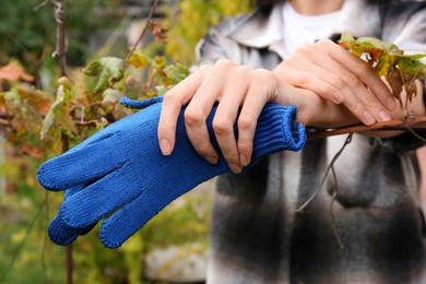Photo of Woman holding blue protective gloves in garden, closeup
